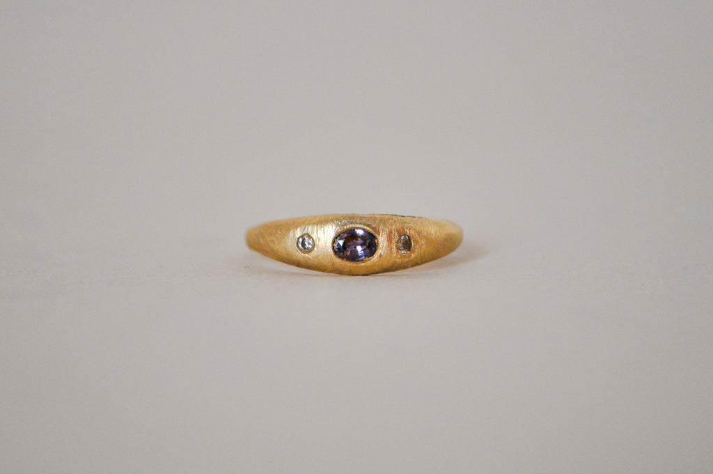 Gold ring with purple sapphire and champagne diamonds on a grey background