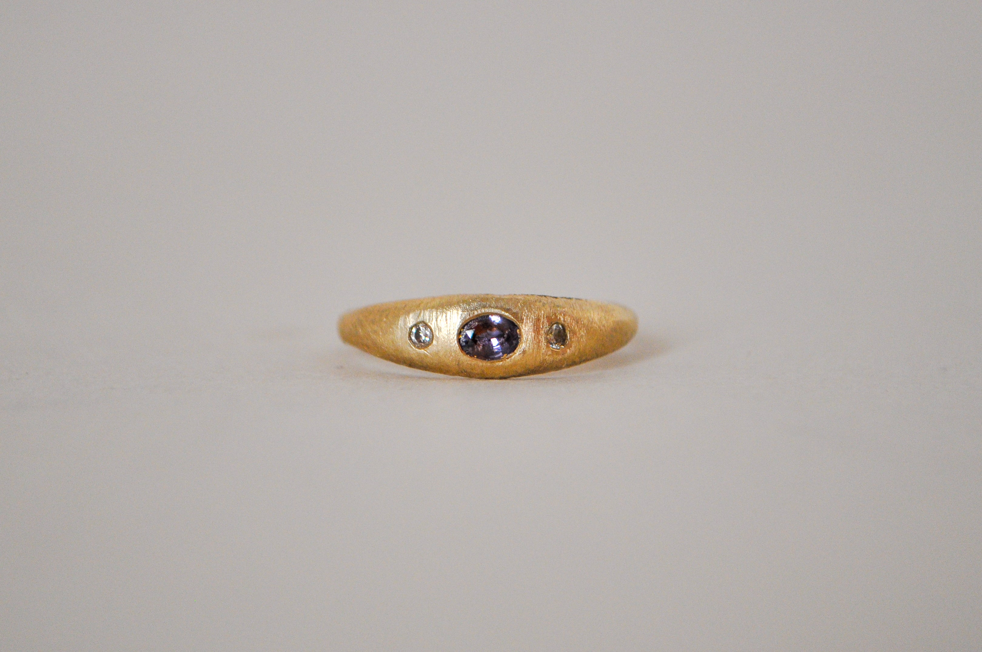 Gold ring with purple sapphire and champagne diamonds on a grey background