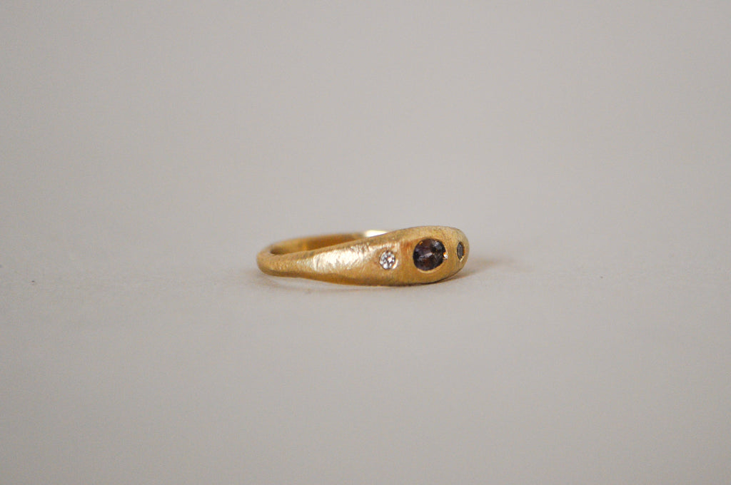Gold ring with purple sapphire and champagne diamonds on a grey background