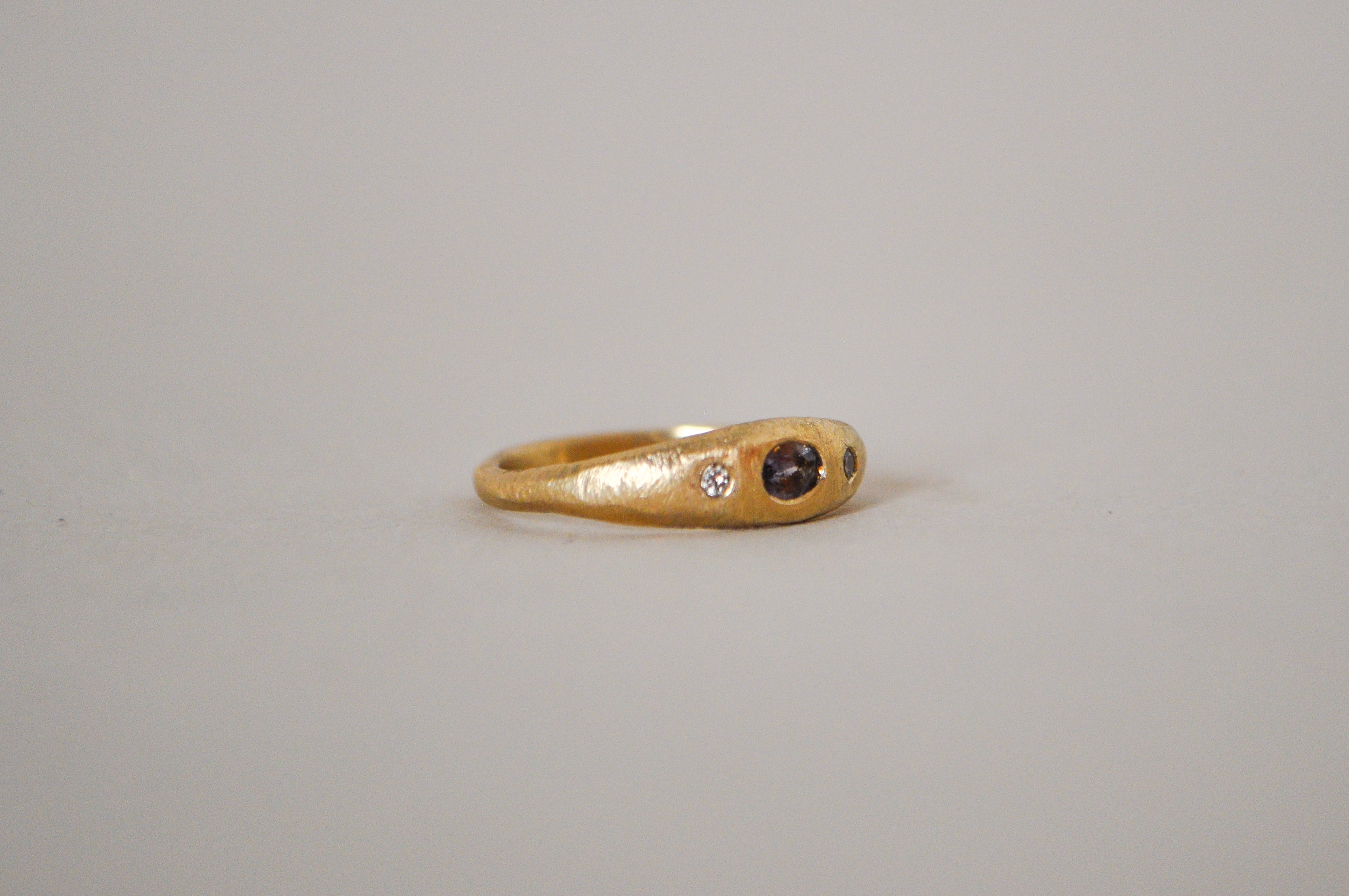 Gold ring with purple sapphire and champagne diamonds on a grey background