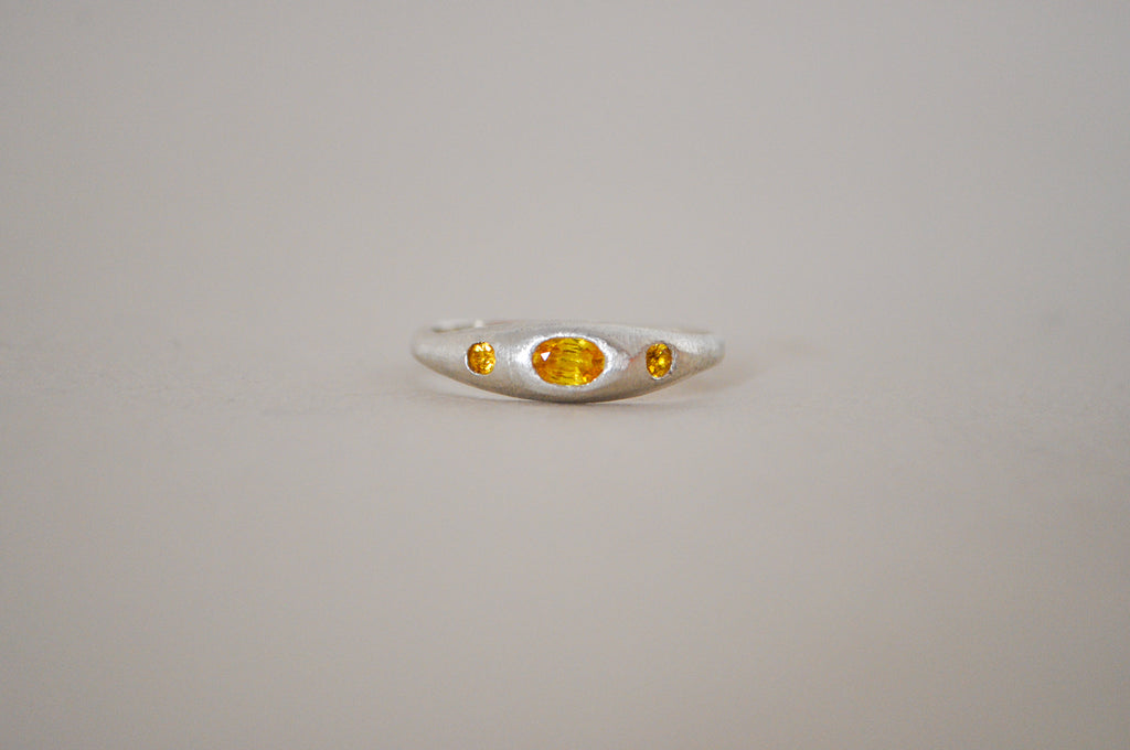 A silver ring featuring a central oval yellow sapphire flanked by two smaller oval yellow sapphire, set against a plain light grey background.
