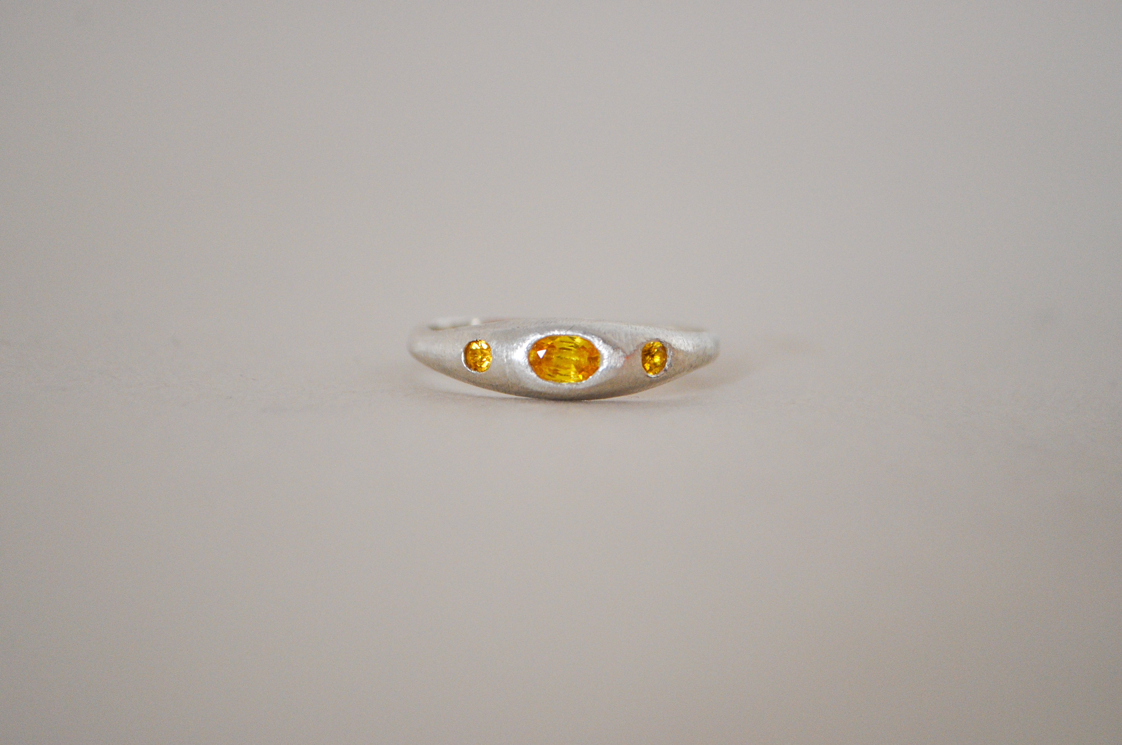 A silver ring featuring a central oval yellow sapphire flanked by two smaller oval yellow sapphire, set against a plain light grey background.