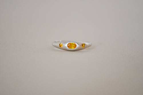 A silver ring featuring a central oval yellow sapphire flanked by two smaller oval yellow sapphire, set against a plain light grey background.