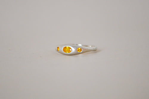 A silver ring featuring a central oval yellow sapphire flanked by two smaller round yellow sapphire, set against a plain light grey background.