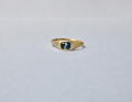 A gold signet ring with a square-cut parti sapphire, displayed on a plain light grey background.