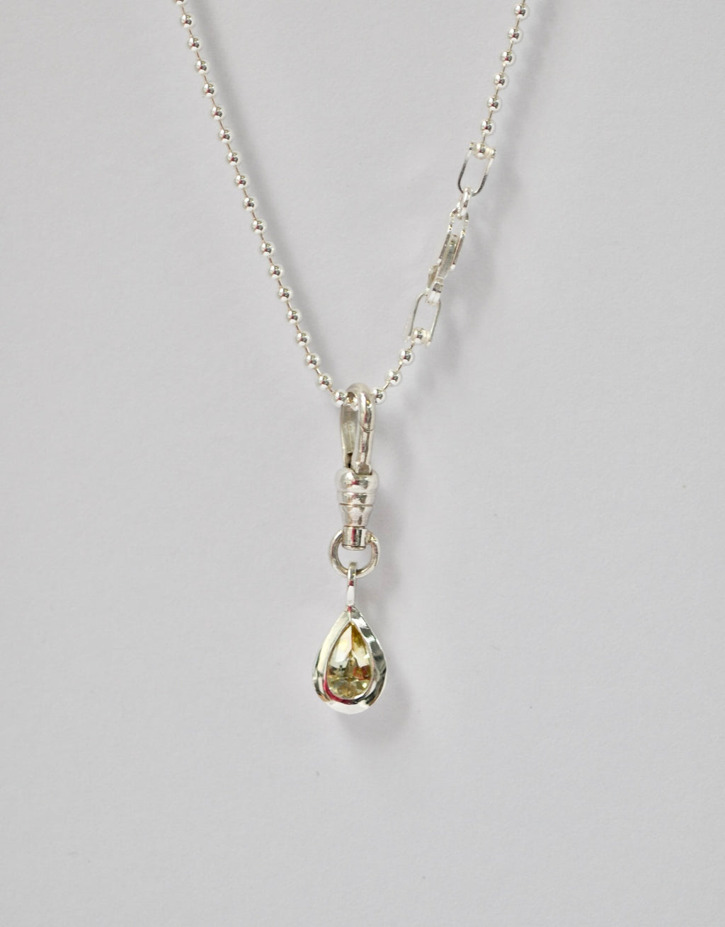Silver necklace with a teardrop-shaped pendant and yellow sapphire on a light grey background