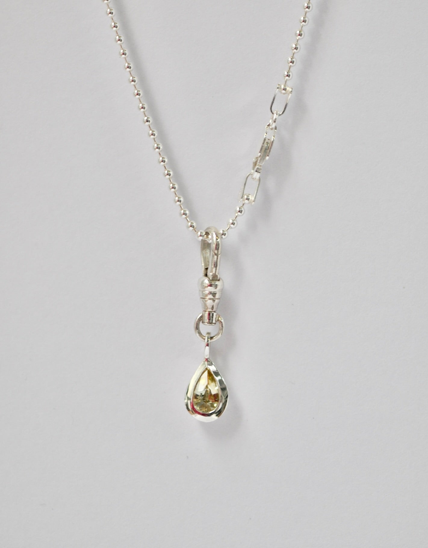 Silver necklace with a teardrop-shaped pendant and yellow sapphire on a light grey background