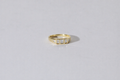 A yellow gold ring with a row of small diamonds, photographed on a plain light gray background.