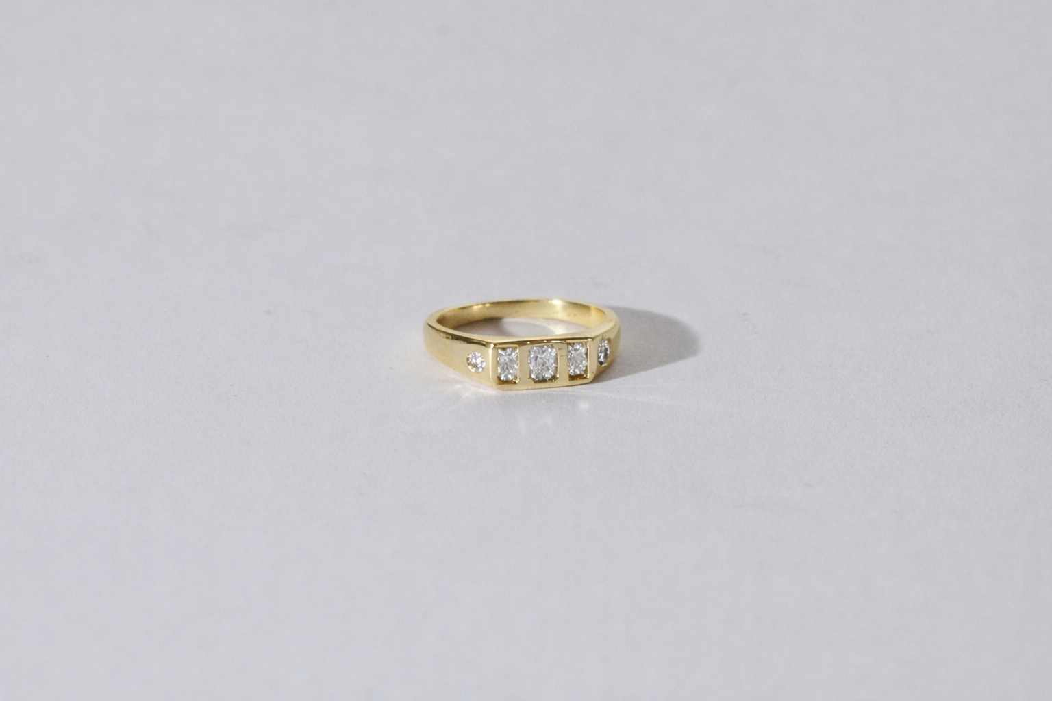 A yellow gold ring with a row of small diamonds, photographed on a plain light gray background.