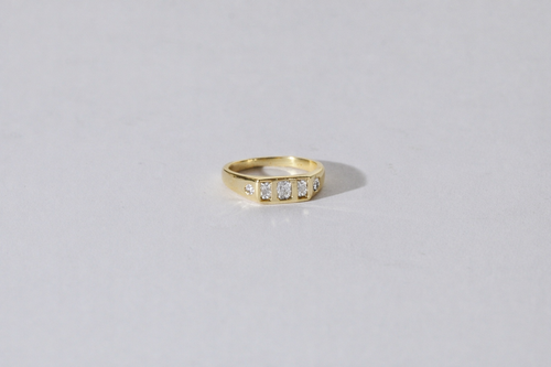 A yellow gold ring with a row of small diamonds, photographed on a plain light gray background.