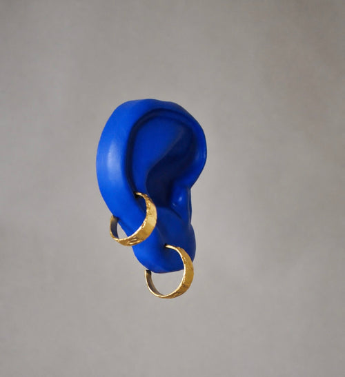 Blue ear model with gold earrings on a grey background