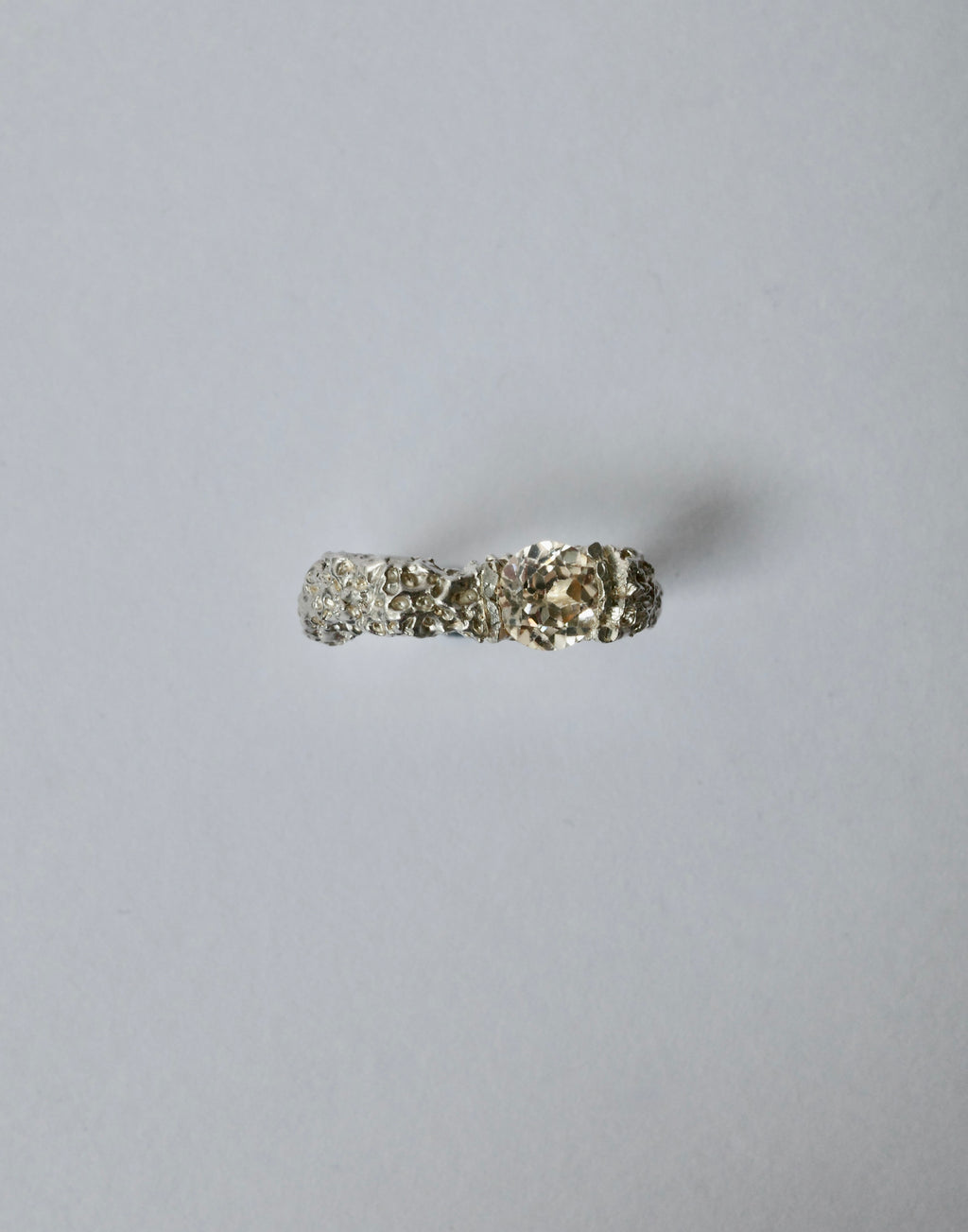 A silver ring with a textured band and a central champagne zircon shown on a plain light grey background.