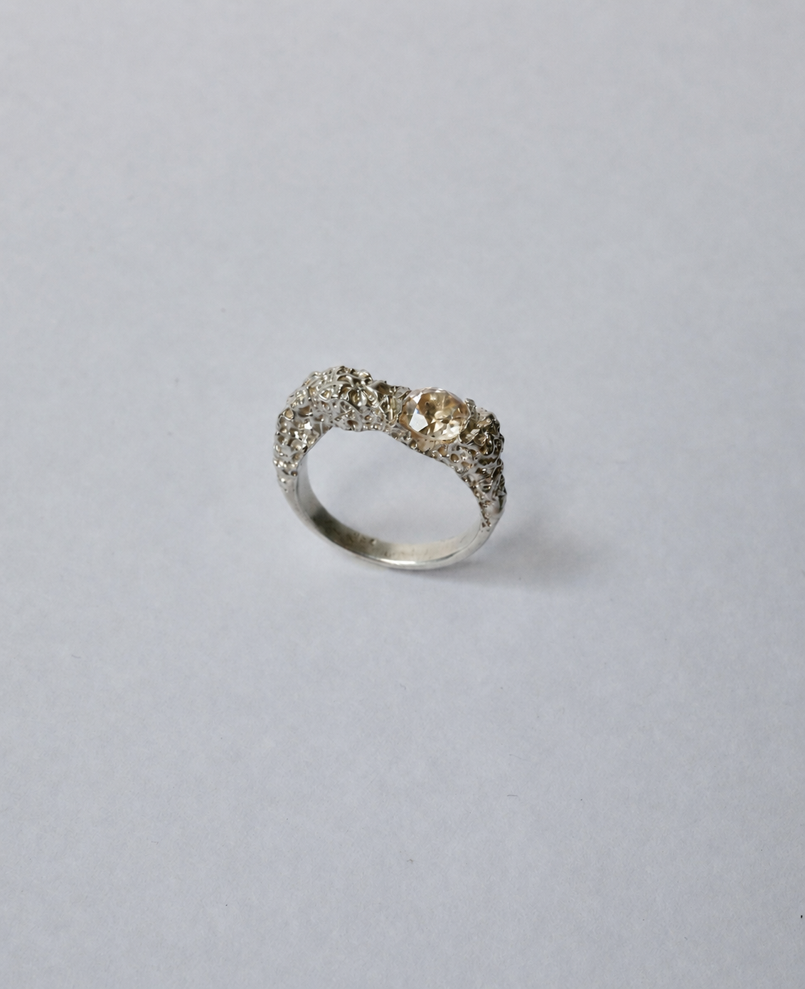 A textured silver ring with a central champagne zircon photographed on a plain light grey background.