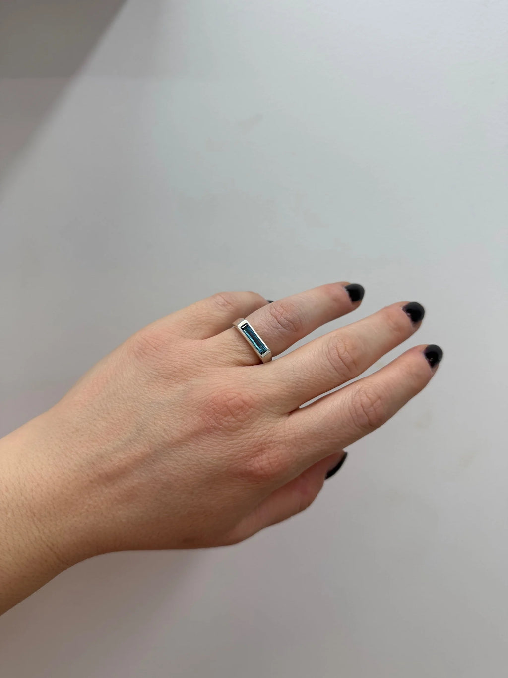 Hand wearing a ring with a London blue topaz on a plain background